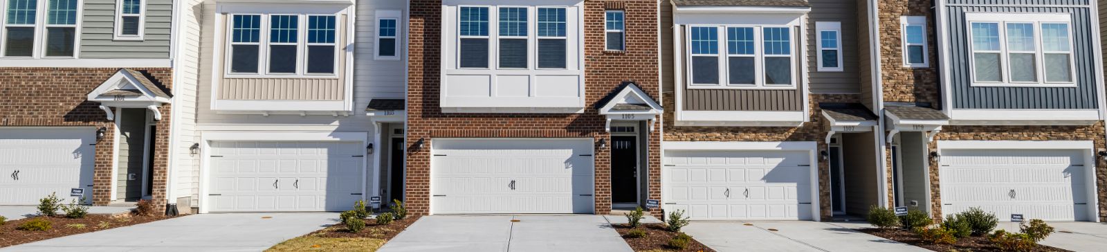 Front view of several modern townhomes in Mound, MN, each featuring clean white sectional garage doors and brick or siding exteriors.