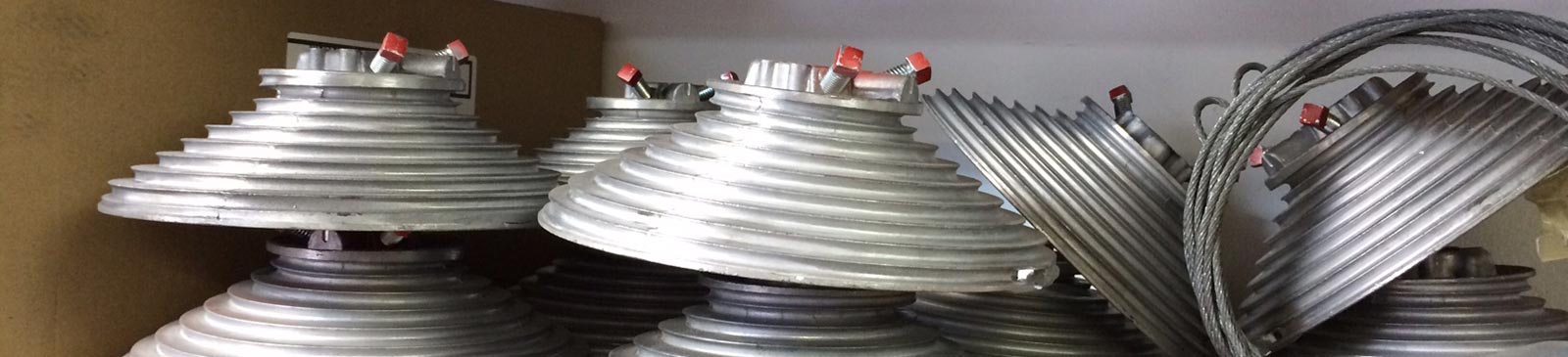 Close-up of stacked metal garage door cable drums and steel cables on a workshop shelf, representing professional garage door repair parts in Mound, MN.