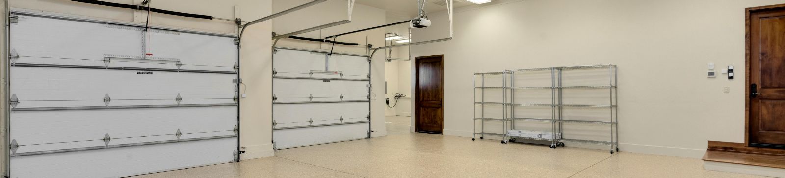 Spacious, modern double garage in Mound, MN, featuring two white sectional overhead doors, ceiling-mounted openers, and organized metal shelving.