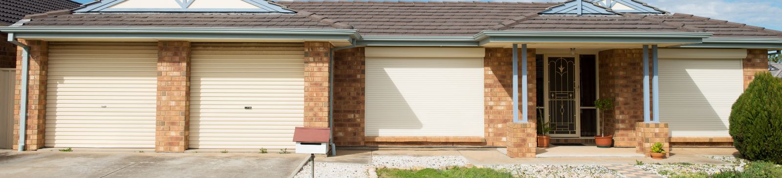 Front view of a brick home in Mound, MN, featuring three closed cream-colored roller garage doors and a tidy driveway.