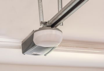 Close-up of a modern automatic garage door opener mounted on the ceiling, showing the rail and motor system in a clean residential garage.