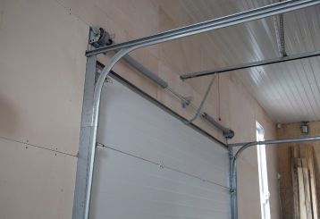Close-up of a white sectional garage door with clean, properly aligned metal tracks and visible torsion spring system inside a well-lit garage.