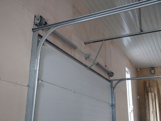 Clean and Aligned Overhead Garage Door Tracks – Maintenance Example Close-up of a white sectional garage door with clean, properly aligned metal tracks and visible torsion spring system inside a well-lit garage.
