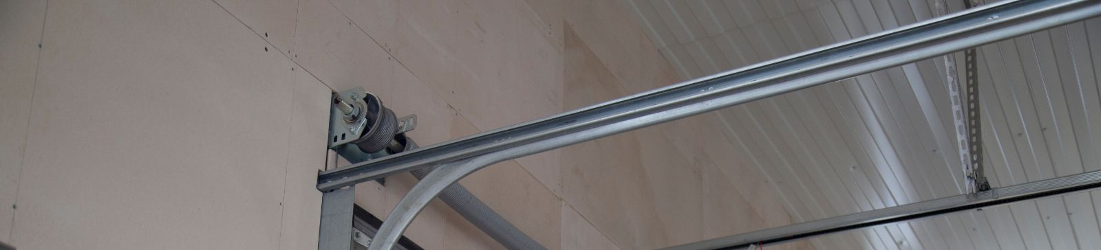 Close-up of a white sectional garage door with clean, properly aligned metal tracks and visible torsion spring system inside a well-lit garage.